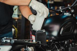 Der Mechaniker ersetzt die Motorradbatterie und hält ein Säurepaket oder ein versiegeltes Batterieelektrolytpaket, um das Auffüllen der Batterie, die Wartung des Motorrads sowie das Service- und Reparaturkonzept vorzubereiten. selektiver Fokus foto