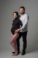 Eine schwangere Frau und ihr Mann umarmen sich auf grauem Hintergrund. Paar erwartet ein Baby. foto