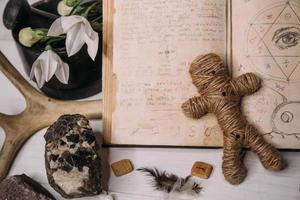 eine voodoo-puppe aus seil liegt mit altem buch grimoire foto