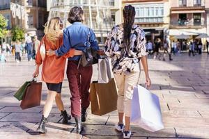 anonyme stilvolle damen, die mit einkaufstüten auf dem platz spazieren foto