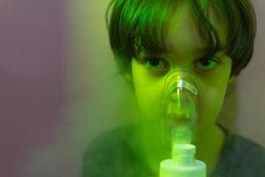 Das Kind inhaliert, der Junge inhaliert das Medikament durch die Maske foto