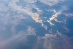 blauer bewölkter himmel am mittag, wenn die sonne von den wolken und gottstrahlen bedeckt ist foto