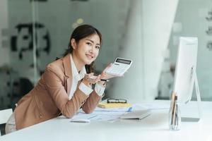 glückliche attraktive asiatische geschäftsfrau, die mit einem laptop und einem finanzdokument im büro arbeitet, erfolgreiche aktion, geschäftskonzept. foto