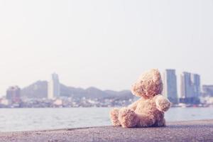 ein brauner, flauschiger teddybär sitzt auf einer einzelnen brücke mit blick auf das meer mit einem kopienraumhintergrund. einsam, Einsamkeit ist sinnlos. foto