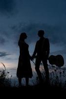 Silhouette eines verliebten Paares bei einem Date. Der Mann hält die Hand des Mädchens. der Typ in Krabben hat eine Gitarre. bei Sonnenuntergang gefilmt. foto