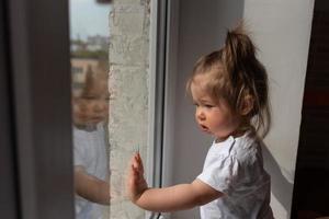 Kleines Mädchen schaut aus dem Fenster und fragt während der durch Coronavirus verursachten Quarantäne nach draußen. foto