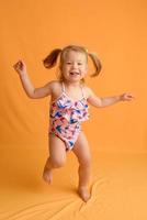 Ein kleines Mädchen im Badeanzug im Alter von anderthalb Jahren springt oder tanzt. das Mädchen ist sehr glücklich. Aufnahme im Studio auf gelbem Hintergrund. foto