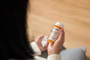 asiatische frau, die pillenrezept liest, wenn sie zu hause grippe auf soaf bekommt foto