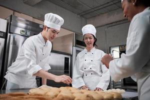 Professionelles Gourmet-Team, drei junge Köche in weißen Kochuniformen und Schürzen kneten Teig und Eier, bereiten Brot und frische Backwaren zu und backen im Ofen in der Restaurantküche aus Edelstahl. foto