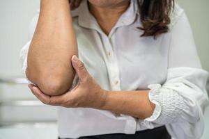 asiatische dame patientin berührt und fühlt schmerzen an ellbogen und arm, gesundes medizinisches konzept. foto