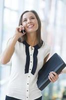 Geschäftsfrau auf Handy hält Ordner und lächelt foto