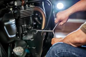mechaniker reparieren motorrad mit schlüssel oder steckdose am motor des motorrads, wartung, reparatur motorradkonzept in der garage