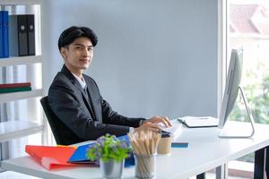 porträt eines asiatischen gutaussehenden mannes, der im büro arbeitet und einen computer auf dem tisch verwendet. foto