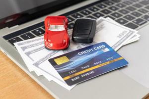kreditkarte, automodell und notizbuch auf holzschreibtisch. Online-Shopping und Autozahlung mit Laptop foto