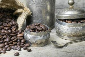 silberne tasse und kaffeebohnen in sackleinentasche auf hölzernem hintergrund foto