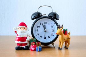 weihnachtsmann und uhr, hirsch und geschenk auf dem tisch. frohes neues jahr und weihnachtskonzept foto