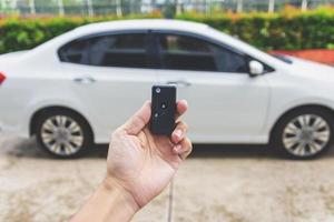 Mann hält Autoschlüssel mit Auto im Hintergrund foto