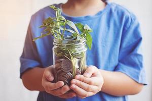 Kind spart Geld in der Flasche Geld, das als Baum aufwächst foto