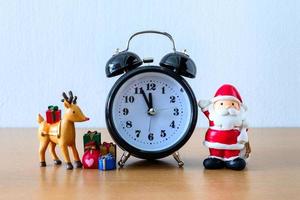 weihnachtsmann und uhr, hirsch und geschenk auf dem tisch. frohes neues jahr und weihnachtskonzept foto