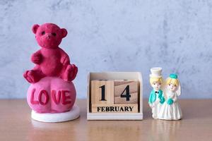 Teddybär und Miniatur-Hochzeitspaar mit Holzkalender 14. Februar. Valentinstag foto