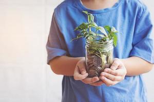 Kind spart Geld in der Flasche Geld, das als Baum aufwächst foto