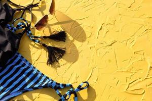 Blau mit schwarzen Streifen weiblicher Badeanzug und Sonnenbrille auf gelbem Hintergrund. das konzept eines strandurlaubs, eines ausflugs ans meer, zubehör zum schwimmen, uv-schutz, bräunen. Exemplar. flachgelegt foto
