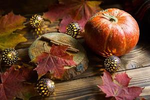 Orangefarbener natürlicher runder Kürbis auf einem Holztisch mit gefallenen gelben und roten Ahornblättern, Zimtstangen. Lichtergirlanden, warme Herbstatmosphäre, Erntedankfest, Erntedankfest, Halloween. Platz kopieren foto