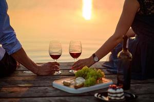 Mann und Frau klirren Weingläser auf dem Hintergrund des farbenfrohen Sommersonnenuntergangs foto