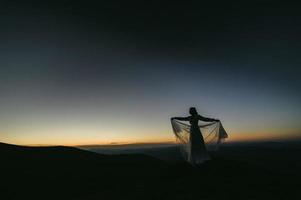 Frau im Hochzeitskleid läuft über das Feld in Richtung der Berge foto
