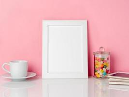 leerer weißer rahmen und süßigkeiten im glas, tasse kaffee oder tee auf einem weißen tisch gegen die rosa wand mit kopierraum foto