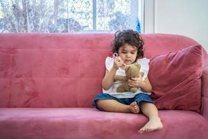 ein kleines süßes mädchen spielt gerne spielzeuginjektionsspritzen spielzeug auf dem teddybär auf dem sofa zu hause, bildungszeit zu hause foto