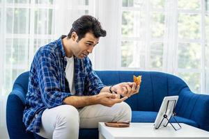 kaukasischer mann zu hause, der zusammen mit ihrer freundin in einer videokonferenz mit digitalem tablet ein stück pizza essen für ein online-treffen in einem videoanruf zur sozialen distanzierung isst foto