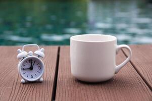 Weißer Wecker auf Holzboden mit Kaffeetasse. Uhr auf 9 Uhr eingestellt. foto