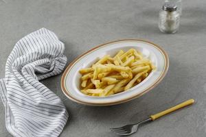 Pommes frites auf Keramikplatte mit Salz und Pfeffer auf Zementgrund foto