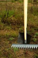 Rechen und Schaufel werden für die Pflanzung im Frühjahr in den Boden gesteckt. Frühling, Gartenpflanzen, Arbeiten auf einem Grundstück, Landschaftsgestaltung, Gartenarbeit, Blumenanbau, Obstkulturen. Platz kopieren foto