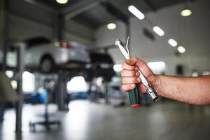 die hand eines automechanikers mit schlüsseln und einem spezialwerkzeug auf dem hintergrund des servicebereichs. ein Mechaniker in einer Autowerkstatt in Uniform. Platz kopieren foto