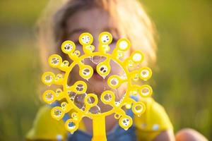 ein mädchen in einem jeansoverall bläst im sommer auf einem feld bei sonnenuntergang seifenblasen. internationaler kindertag, glückliches kind, outdoor-aktivitäten. sommer hintergrund. gesunder und umweltfreundlicher Lebensstil foto