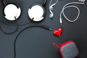 ein herzförmiger Kopfhörersplitter für ein verliebtes Paar. verbunden mit einem roten tragbaren Lautsprecher und zwei Kopfhörern - flach liegend. valentinstag, liebe, moderne technologie, kopierraum, schwarzer hintergrund foto