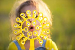 ein mädchen in einem jeansoverall bläst im sommer auf einem feld bei sonnenuntergang seifenblasen. internationaler kindertag, glückliches kind, outdoor-aktivitäten. sommer hintergrund. gesunder und umweltfreundlicher Lebensstil foto