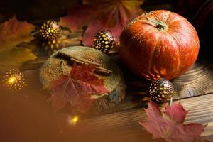 Orangefarbener natürlicher runder Kürbis auf einem Holztisch mit gefallenen gelben und roten Ahornblättern, Zimtstangen. Lichtergirlanden, warme Herbstatmosphäre, Erntedankfest, Erntedankfest, Halloween. Platz kopieren foto