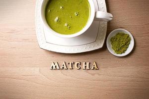 japanischer Matcha-Grüntee wird in einen weißen Becher und auf eine weiße Untertasse in Pulverform gegossen. Inschrift in Holzbuchstaben in Englisch. Teeservice, belebendes Getränk, Vitalität, Antioxidans. Platz für Text foto