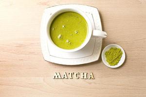 japanischer Matcha-Grüntee wird in einen weißen Becher und auf eine weiße Untertasse in Pulverform gegossen. Inschrift in Holzbuchstaben in Englisch. Teeservice, belebendes Getränk, Vitalität, Antioxidans. Platz für Text foto