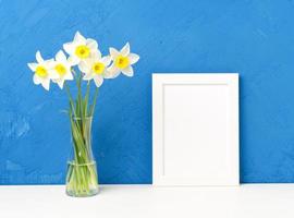 Strauß frischer Blumen, Narzissen in Vase auf weißem Tisch, gegenüber blau strukturierter Betonwand foto