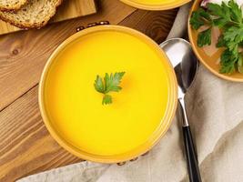 braune Schüssel Kürbissuppe mit Petersilie auf braunem, dunklem Holzhintergrund, Draufsicht, Nahaufnahme foto