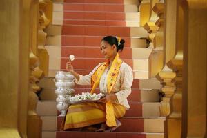 Junges asiatisches Mädchen in traditioneller burmesischer Tracht, das eine Schüssel Reis in der goldenen Pagode im Tempel von Myanmar hält. myanmarer frauen, die blumen mit birmanischer traditioneller kleidung halten, die einen buddhistischen tempel besuchen foto