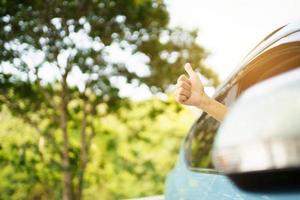 nicht erkennbare ältere erwachsene Frau, die einen Daumen nach oben außerhalb der Windschutzscheibe oder des Fensters der Fahrzeugseite mit Kopienraum zeigt. Fröhliches Fahr- und Reisekonzept. foto