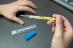 Frauenhand, die klinisches Thermometer auf dem Schreibtisch hält, nachdem sie das klinische Thermometer verwendet und sich Sorgen über die Ausbreitung des Coronavirus gemacht hat foto