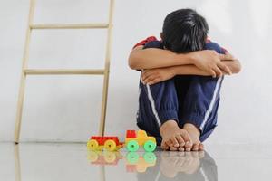 Trauriges und einsames Kind, das mit seinem Spielzeug auf dem Boden an der Wand sitzt. traumatische Erfahrung in der Kindheit, Psychologie, psychisch, Asperger-Syndrom, Asperger-Störung, Autismus, Autismus. foto