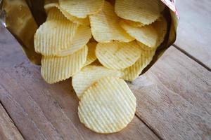 geöffnete Packung mit Kartoffelchips über Holztisch foto