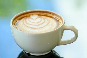 Latte Art Kaffeetasse auf Glastisch. unscharfer Blattreflexionshintergrund. foto